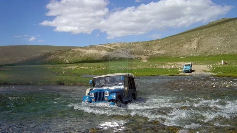 An old model jeep crossing a river in Skardu
